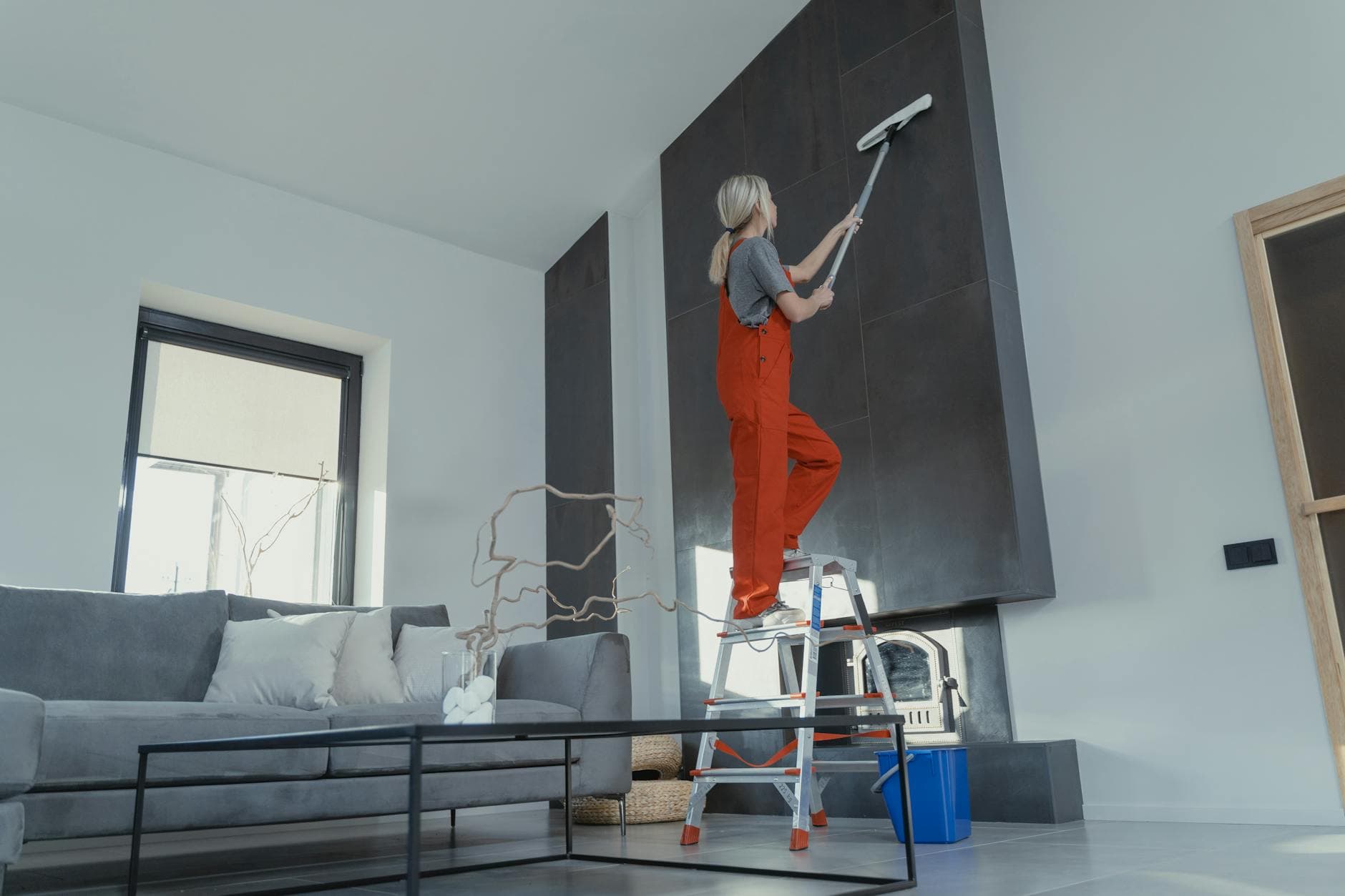 Connecticut Maid cleaner in red overalls on a ladder cleaning a high wall in a Connecticut apartment — Office Cleaning in Ridgefield, Fairfield County