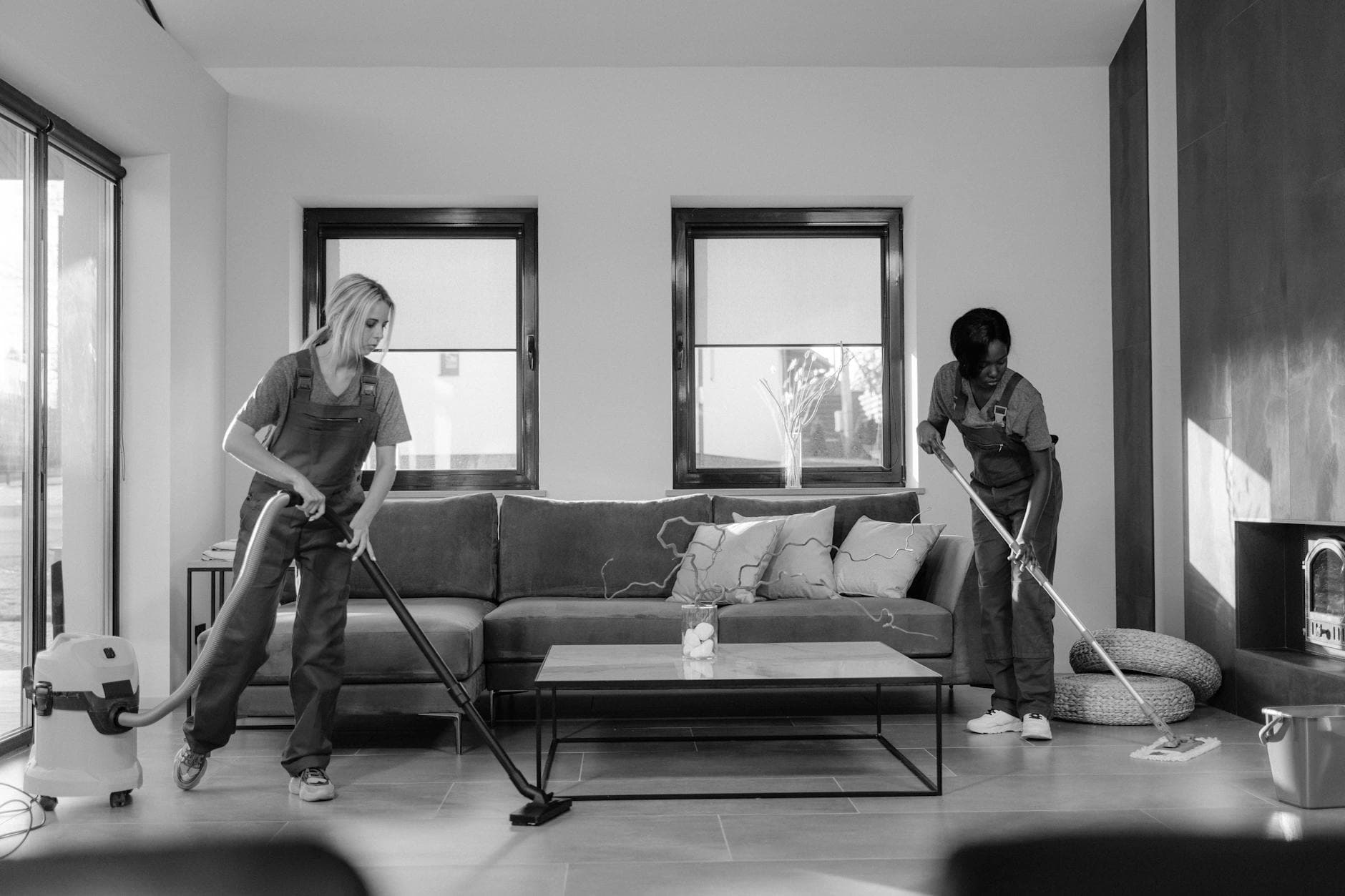 Two Connecticut Maid cleaners in work uniforms using a vacuum and mop in a modern Connecticut living room — Office Cleaning in Norwalk, Fairfield County